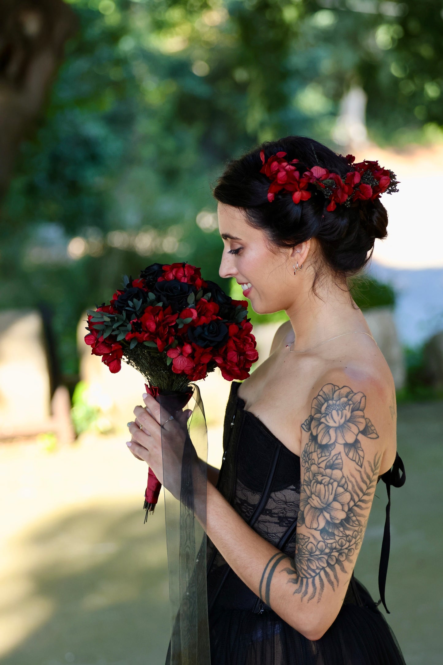 Novia con corona de flores sosteniendo ramo de rosas rojas y negras con hojas verdes oscuras, estilo gótico y sofisticado