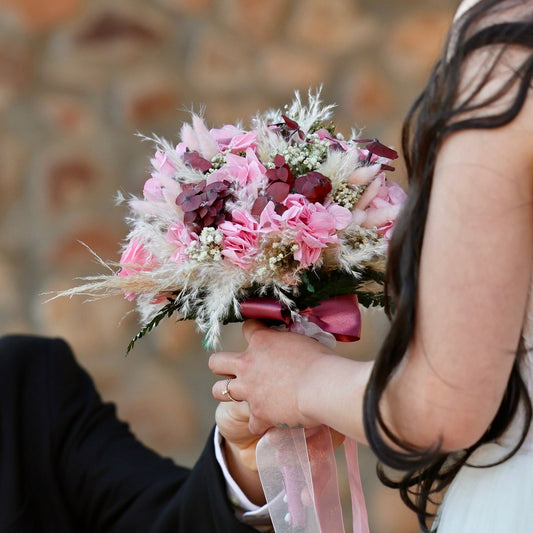Novios sosteniendo ramo de novia preservado con rosas rosadas, flores secas beige y burdeos, estilo romántico y atemporal