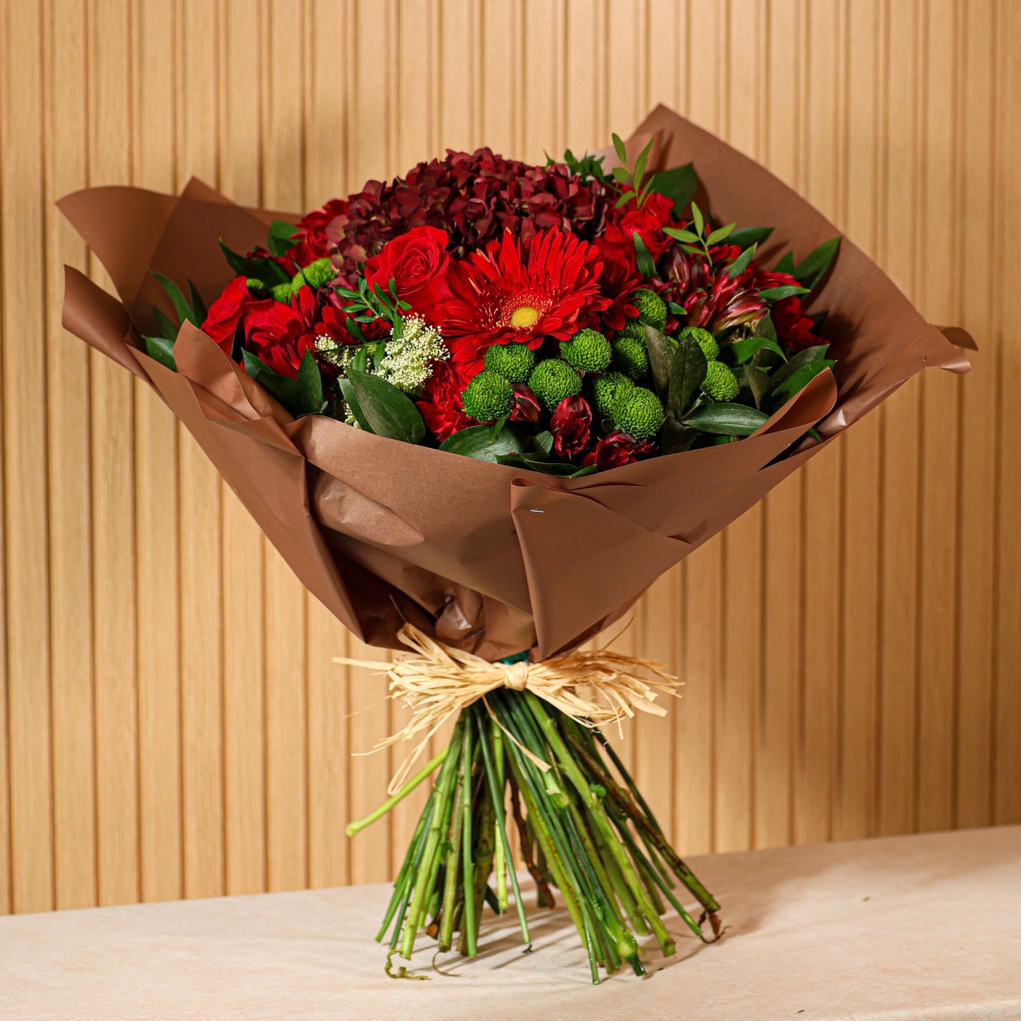 Ramo de flores con rosas rojas, gerberas rojas y hortensias rojizas sobre fondo verde