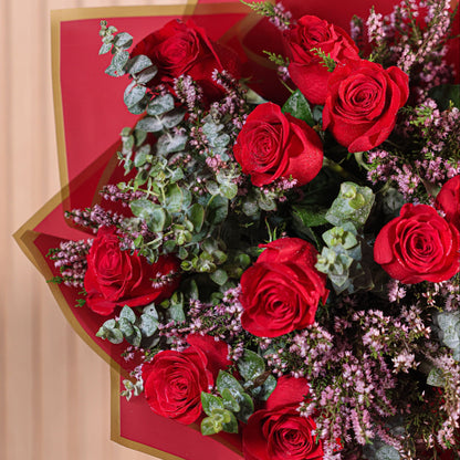 Detalle de ramo de 12 rosas rojas con eucalipto y brezo morado sobre fondo neutro, ideal para decoración o regalo floral duradero