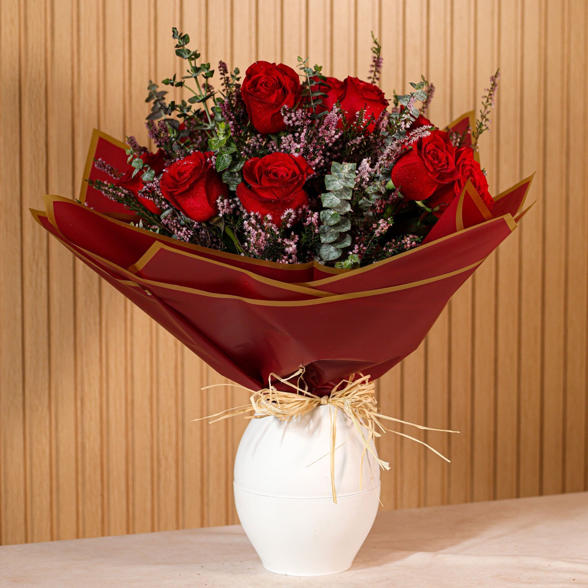 Ramo de 12 rosas rojas con eucalipto y brezo morado sobre fondo neutro, ideal para decoración o regalo floral duradero