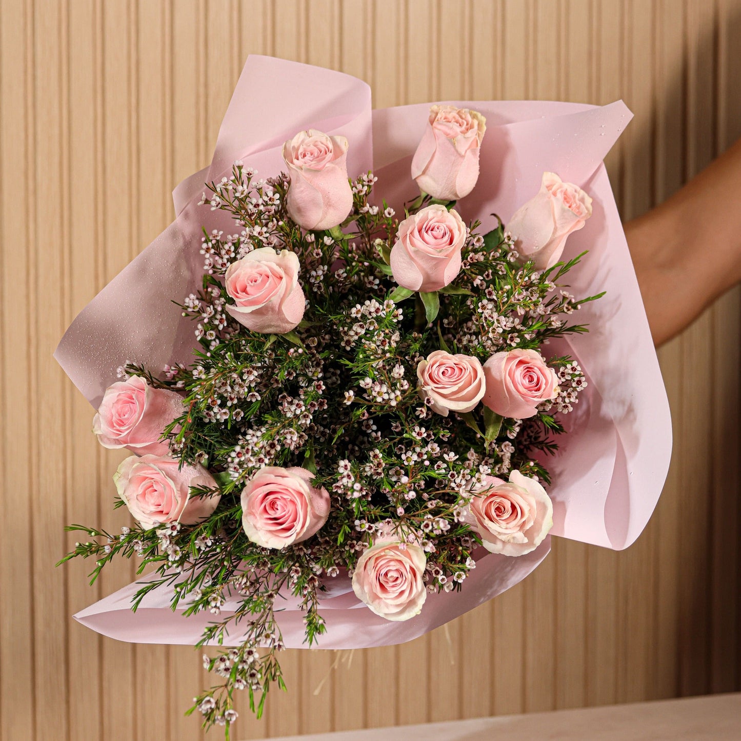 Ramo de 12 rosas rosadas con eucalipto y flor de cera sobre fondo neutro