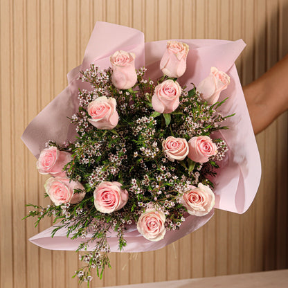 Ramo de 12 rosas rosadas con eucalipto y flor de cera sobre fondo neutro