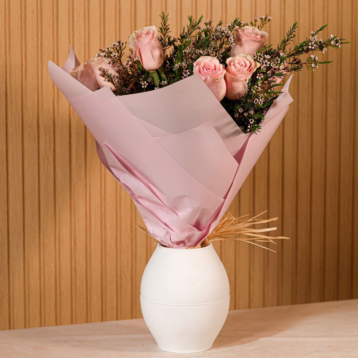 Ramo de 12 rosas rosadas con eucalipto y flor de cera sobre fondo neutro