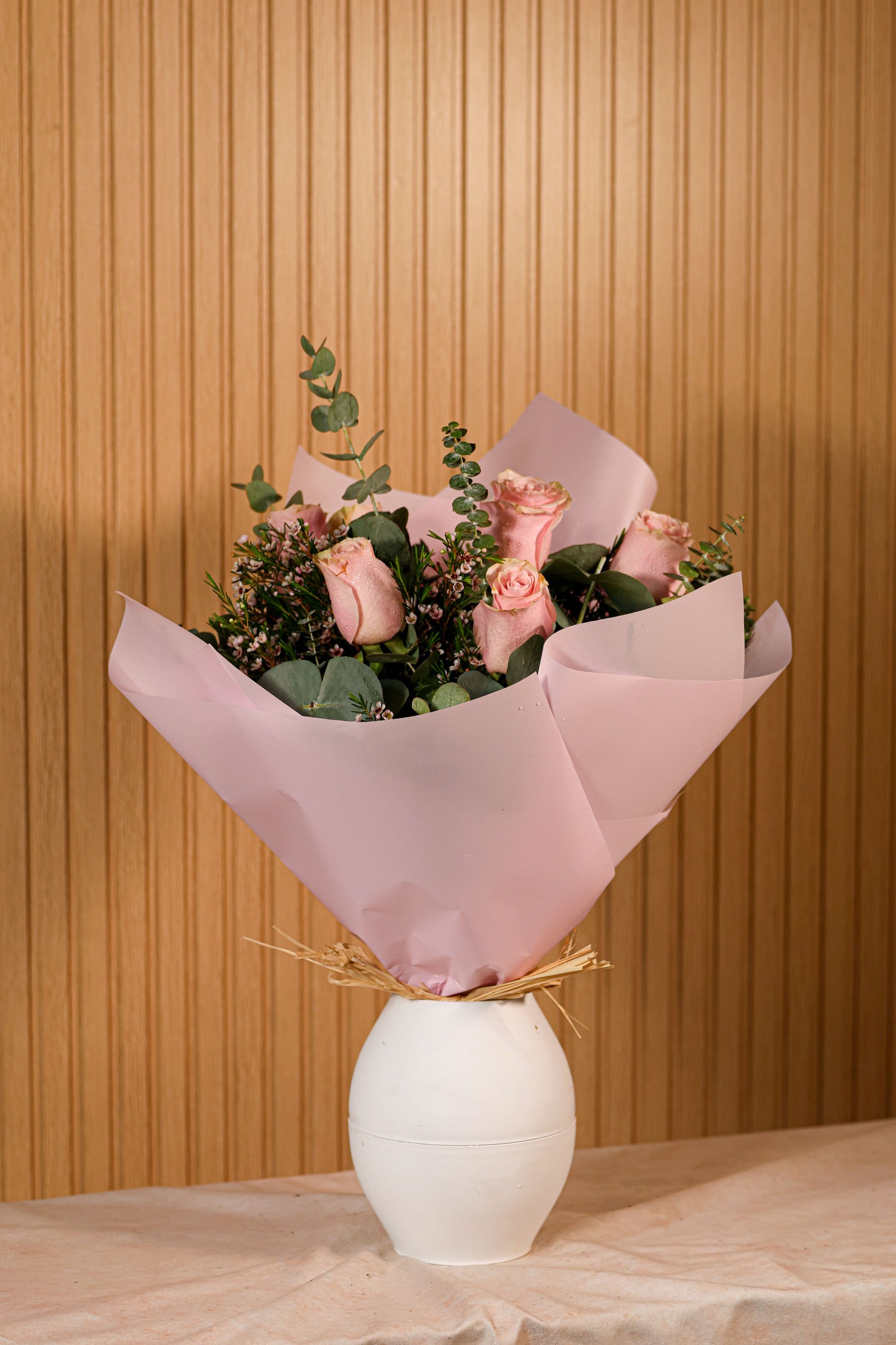 Ramo de 6 rosas rosadas con eucalipto y flor de cera sobre fondo neutro, ideal para decoración o regalo floral duradero