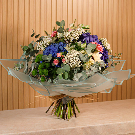 Ramo de flores preservadas Aqua Belle con hortensias azules, gerberas blancas, rosas spray rosadas y eucalipto verde