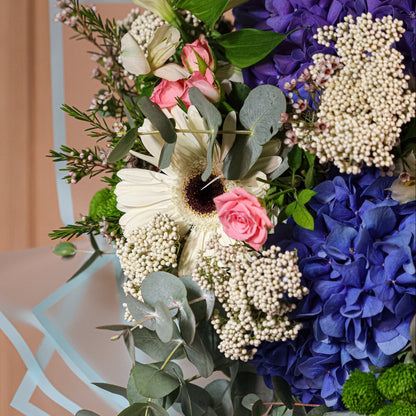 Ramo de flores preservadas Aqua Belle con hortensias azules, gerberas blancas, rosas spray rosadas y eucalipto verde
