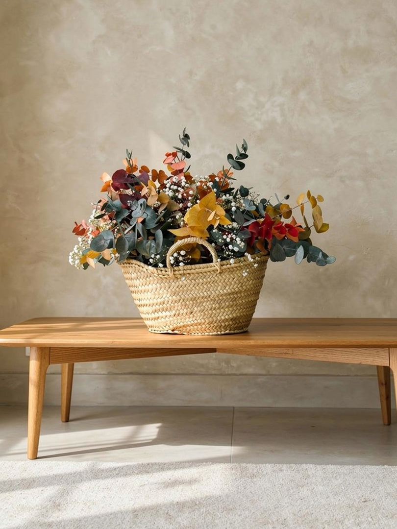 Composición de flores preservadas en cesta de mimbre con tonos ocres, verdes y blancos en madera