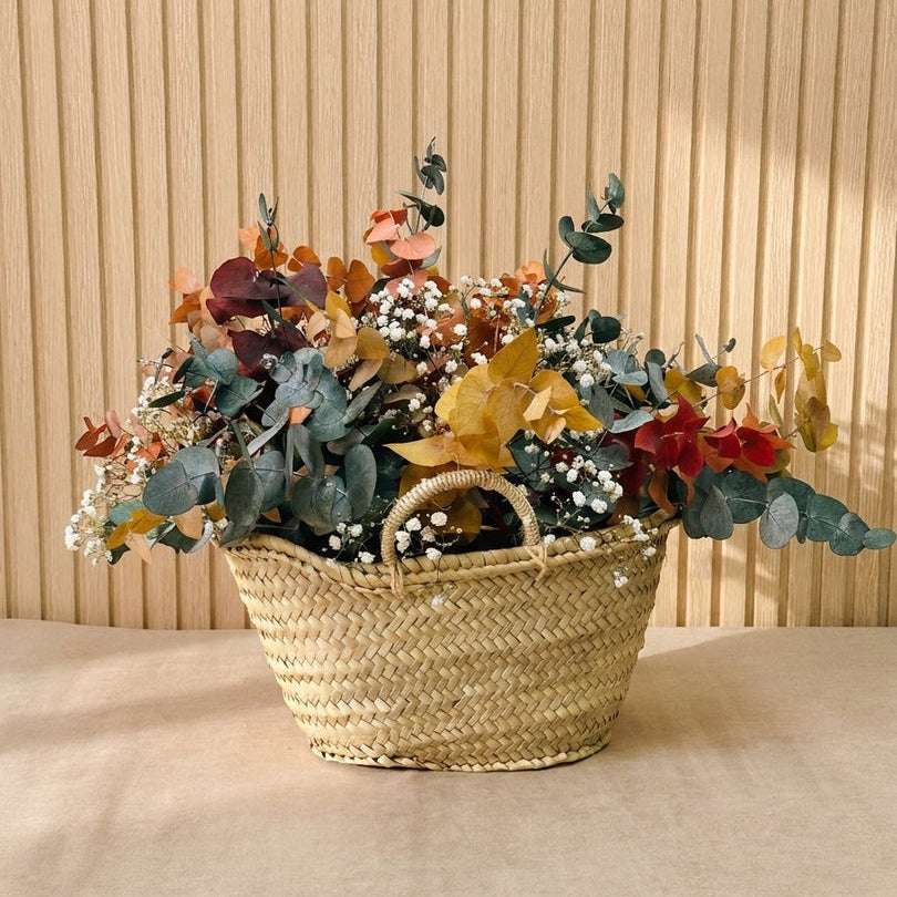 Composición de flores preservadas en cesta de mimbre con tonos ocres, verdes, y blancos